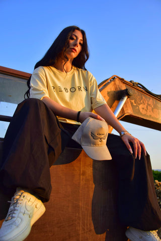 ragazza mora con indosso maglia reborn beige con scritta nera e in mano un cappello beige con scritta nera